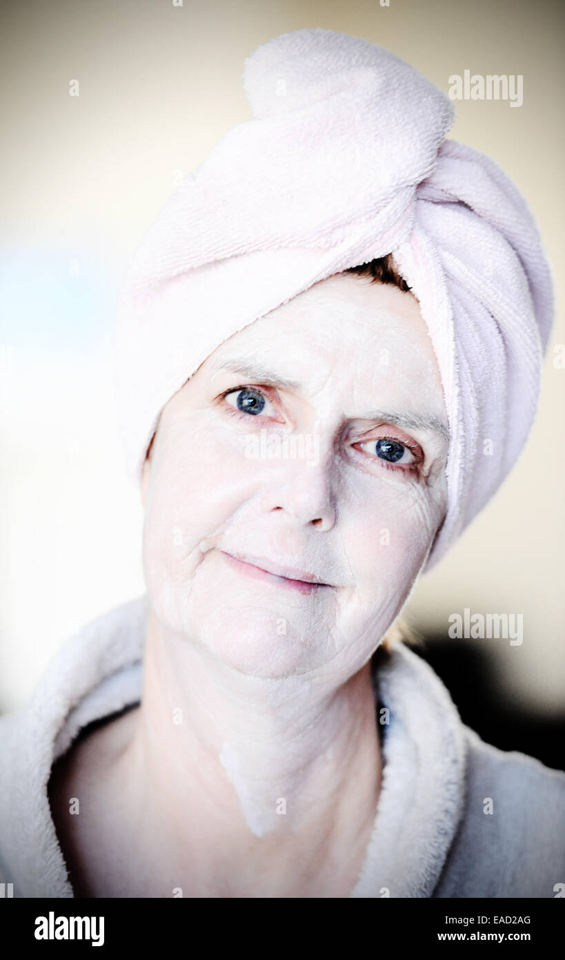 Donna di mezza età donna che indossa un turbante sui capelli bagnati e utilizzando una salute e bellezza viso pack per la pelle Foto Stock