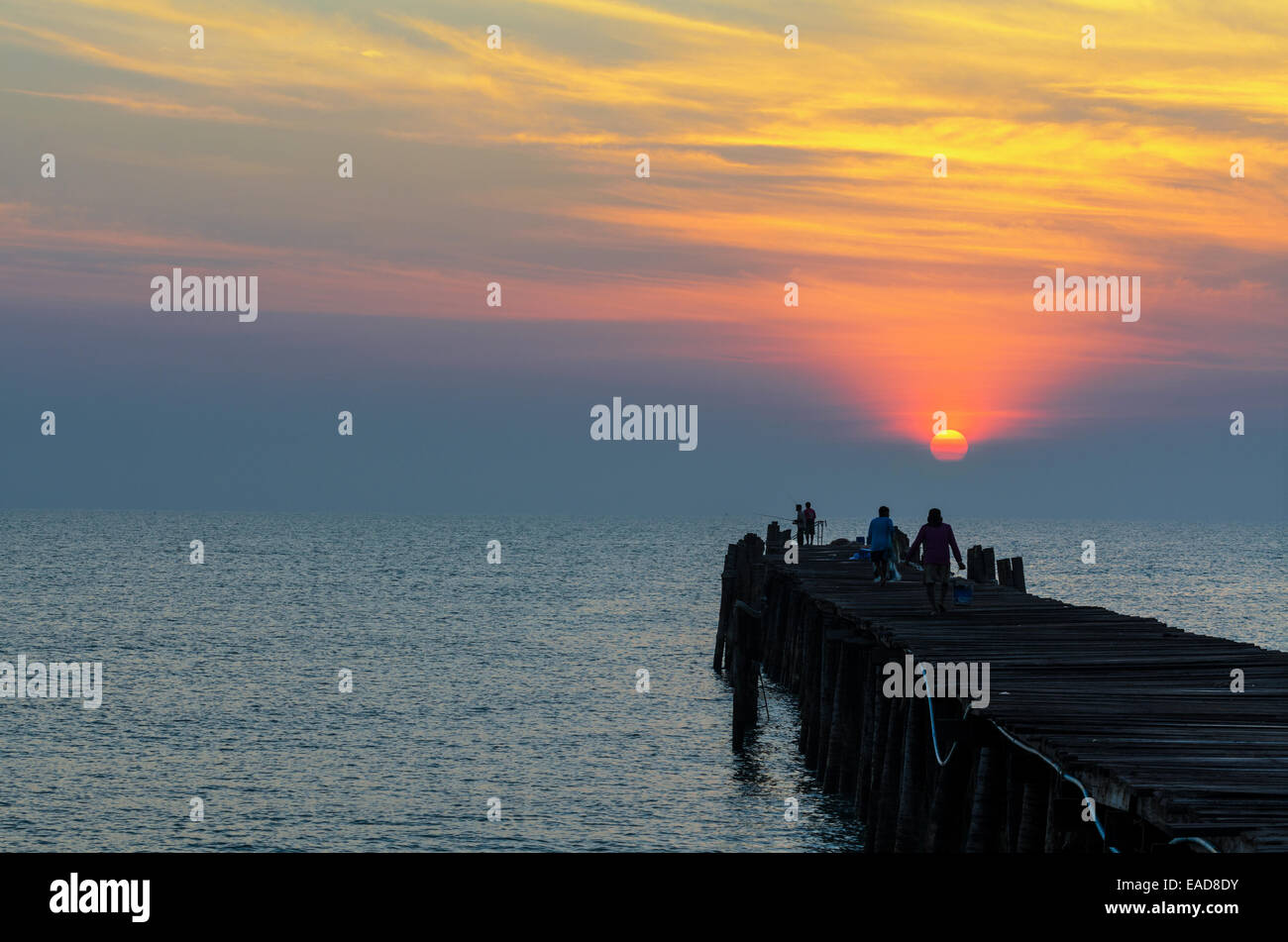 Silhouette pescatore sul vecchio ponte di legno e il mare a sunrise in zone rurali della Thailandia. Foto Stock