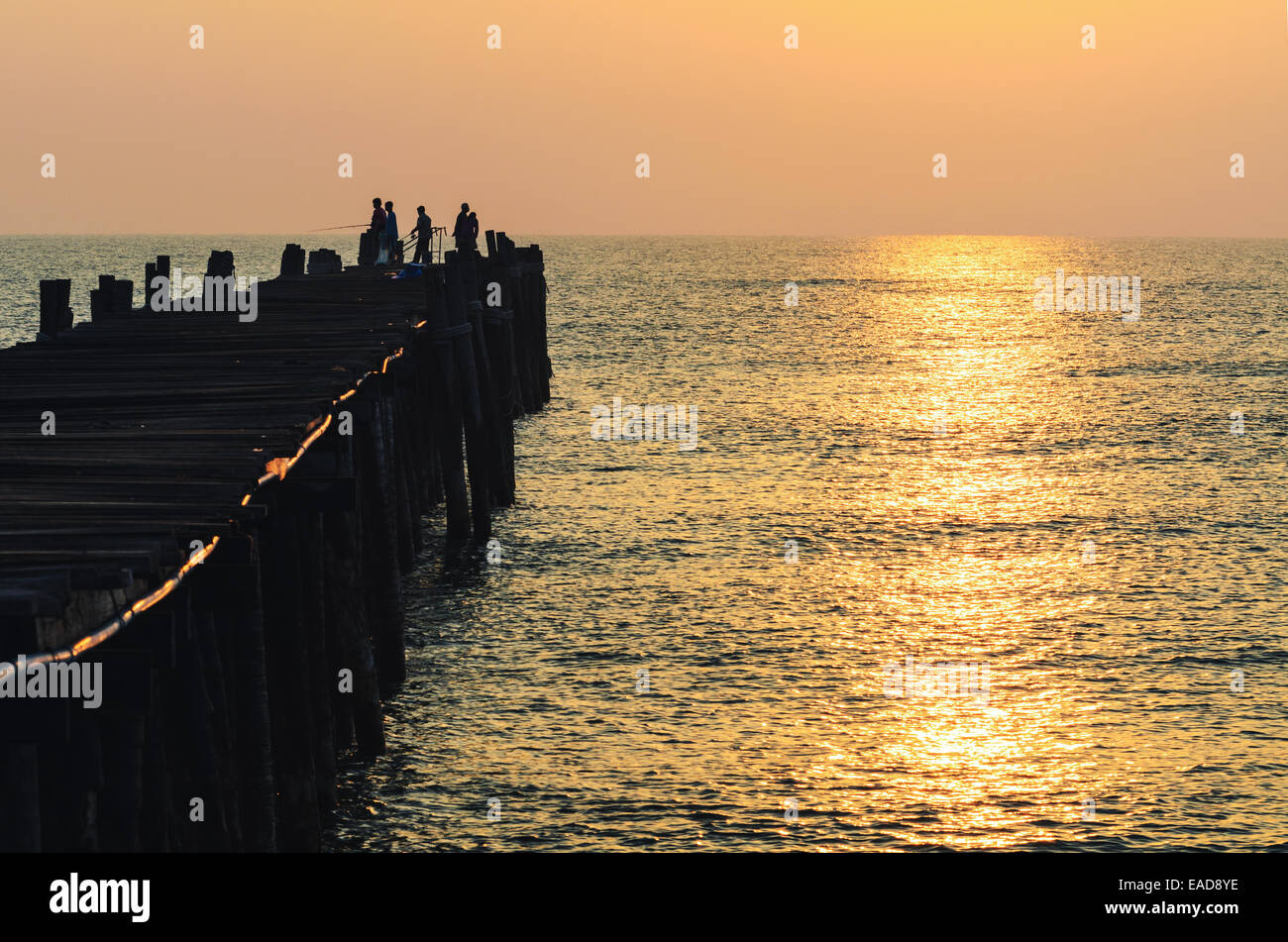 Silhouette pescatore sul vecchio ponte di legno e il mare a sunrise in zone rurali della Thailandia. Foto Stock