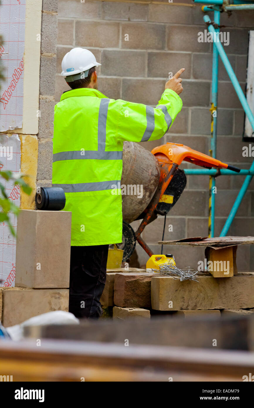Builder lavora in un cantiere che indossa un giubbetto alta visibilita e bianco elmetto casco di protezione Foto Stock