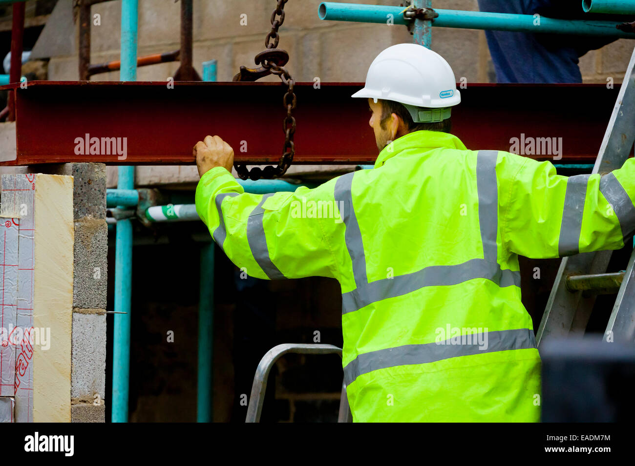 Builder collabora con trave metallica su un cantiere che indossa un giubbetto alta visibilita e bianco elmetto casco di protezione Foto Stock