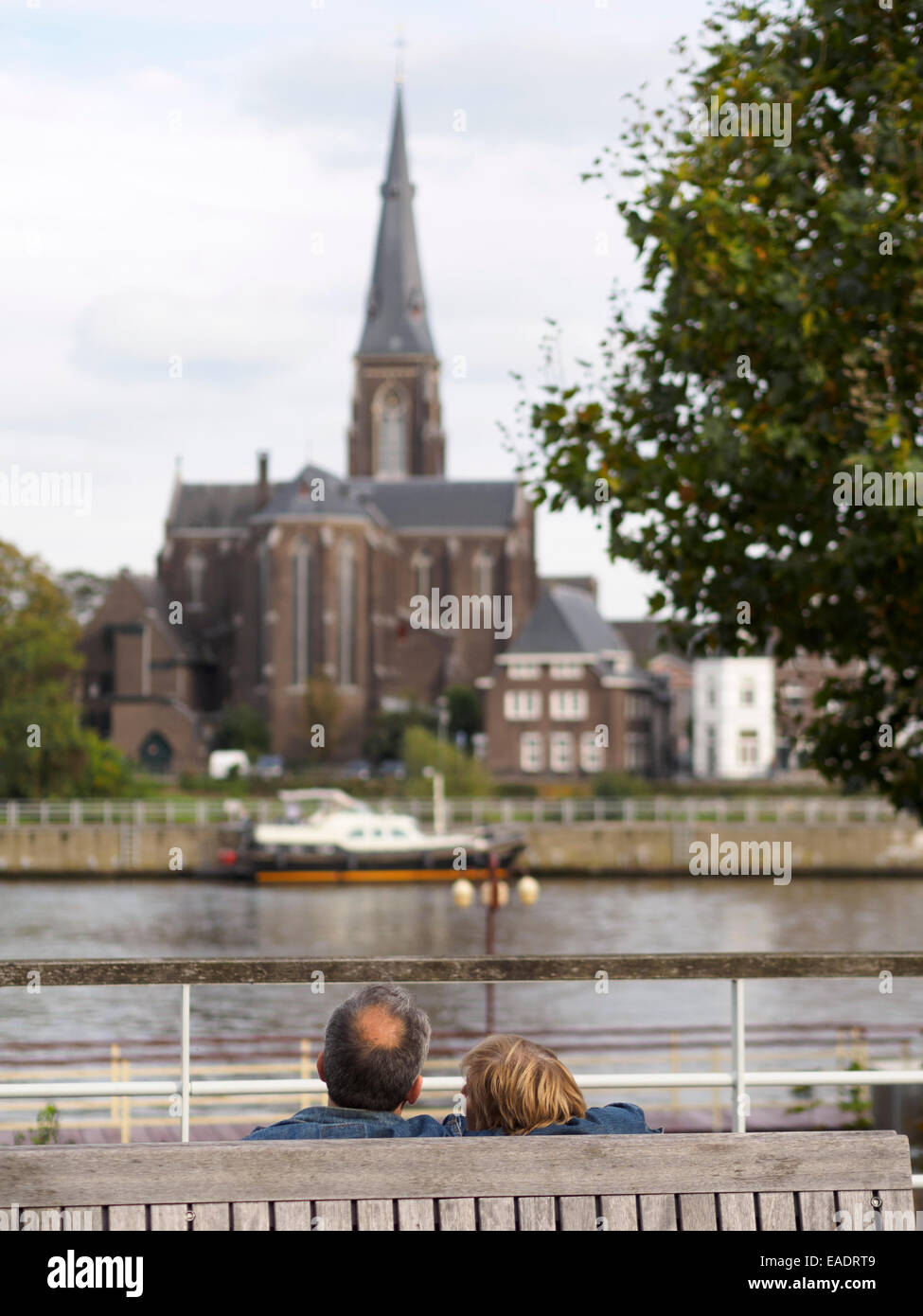 Coppia di mezza età che abbraccia su una panchina nel parco di fronte al fiume Maas e il San Martinus chiesa torre a Maastricht, Olanda Foto Stock