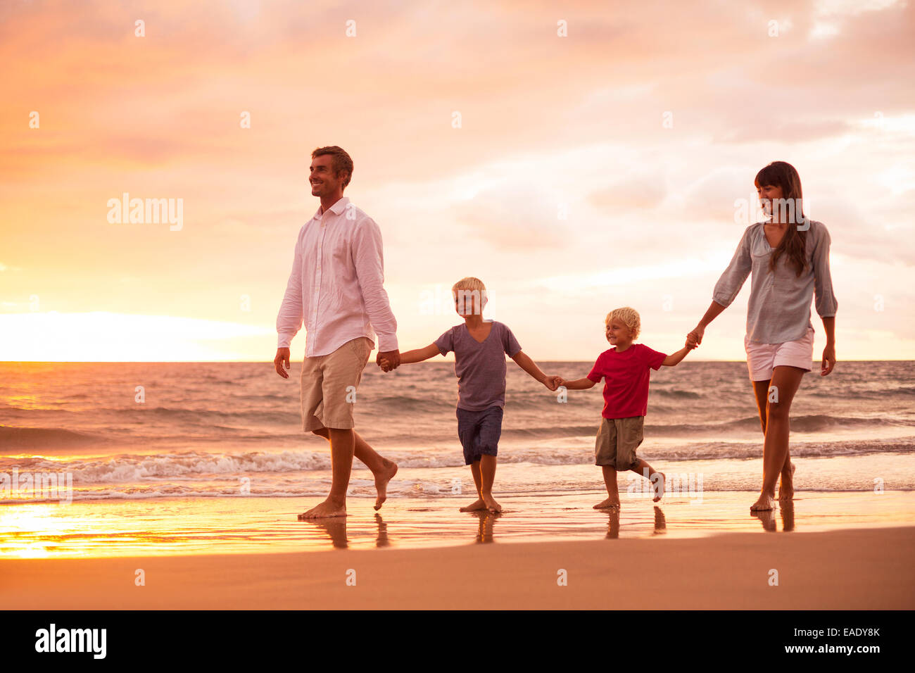 Felice famiglia giovane di quattro sulla spiaggia al tramonto Foto Stock