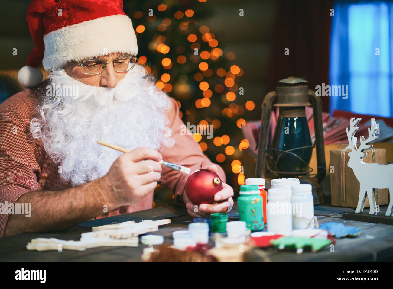 Senior uomo in Santa il cappello e la barba di pittura sfere giocattolo con gouache Foto Stock