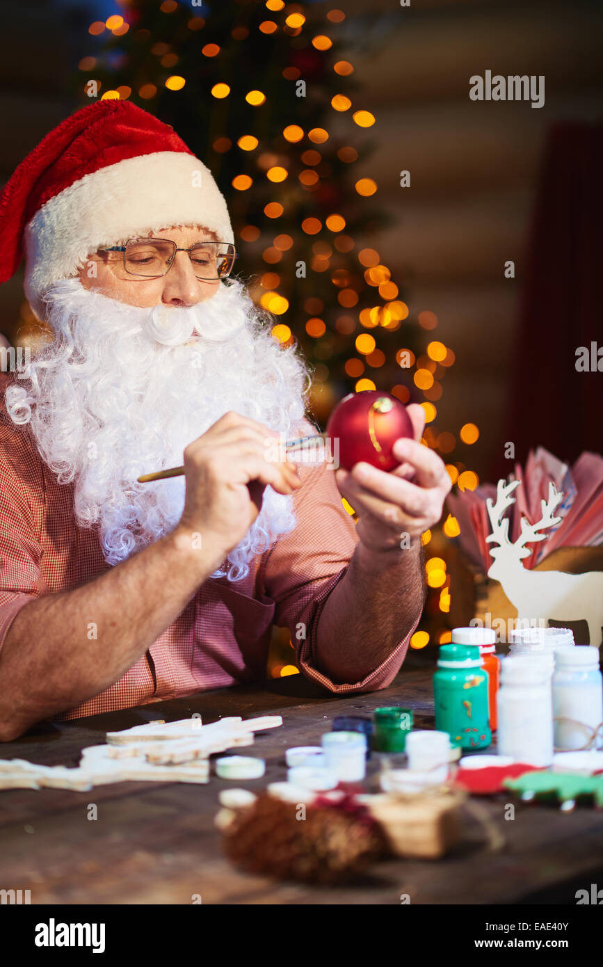 Senior uomo in Santa il cappello e la barba di pittura palla giocattolo con gouache prima di natale Foto Stock
