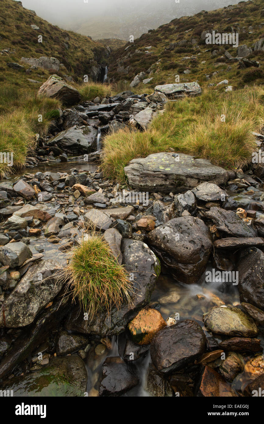 Un flusso crea una serie di cascate mini come esso fluisce in Llyn Idwal in una nebbiosa mattina in Snowdonia, Gwynedd, il Galles del Nord Foto Stock