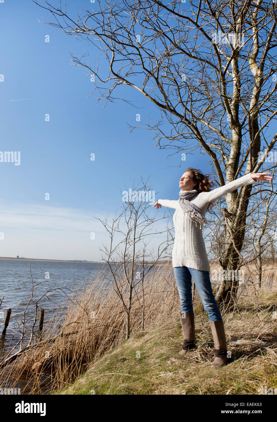 Una donna in piedi sulla riva di un lago e godersi il sole in inverno Foto Stock