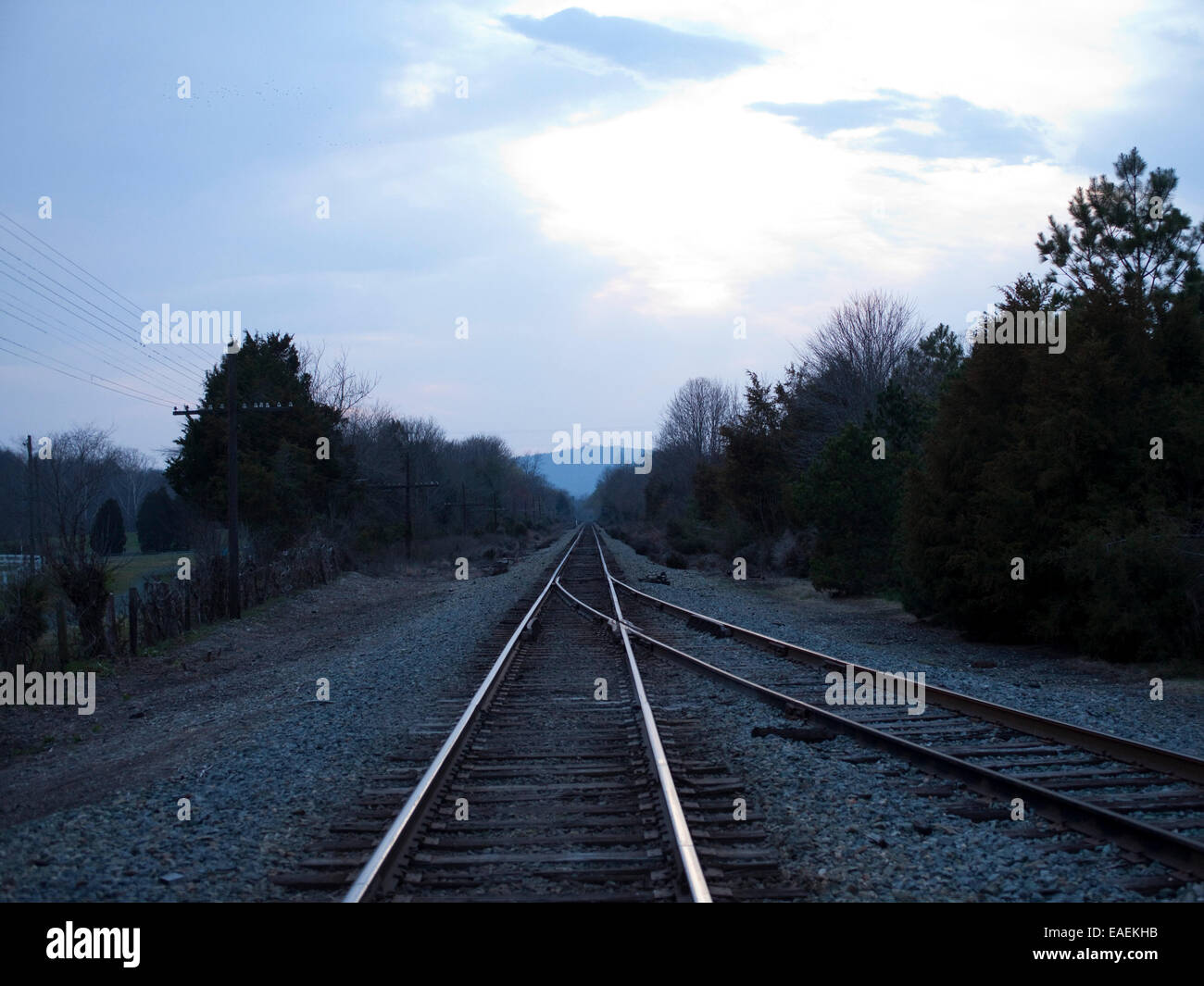 Binari del treno al crepuscolo e sfuggente in il paesaggio rurale. Foto Stock