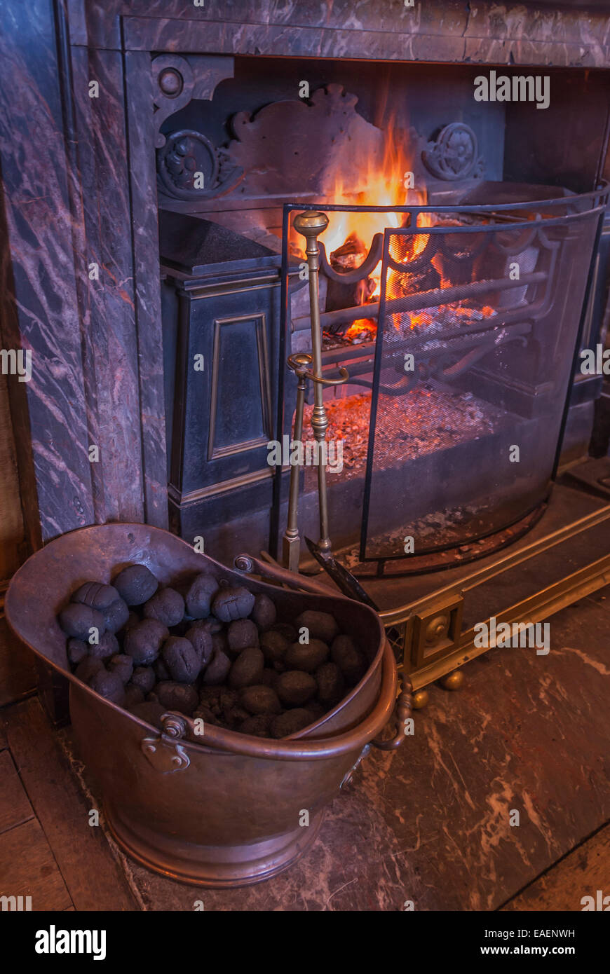 Uno scoppiettante fuoco aperto in una casa di campagna con un carbone di ottone grembiale sulla suola e un caminetto in marmo Foto Stock
