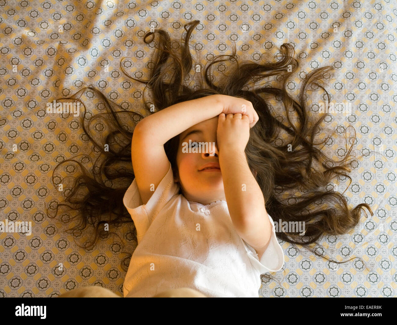 Ragazza giovane con un sacco di capelli facendo una faccia buffa mentre giaceva sul letto Foto Stock