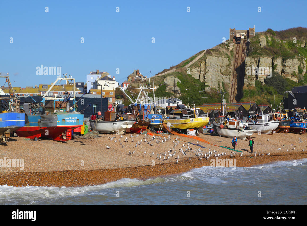 Coppia a piedi sulla spiaggia di Hastings Old Town Stade, di fronte alle barche da pesca e la Galleria d'Arte Contemporanea di Hastings, East Sussex, Regno Unito. Foto Stock