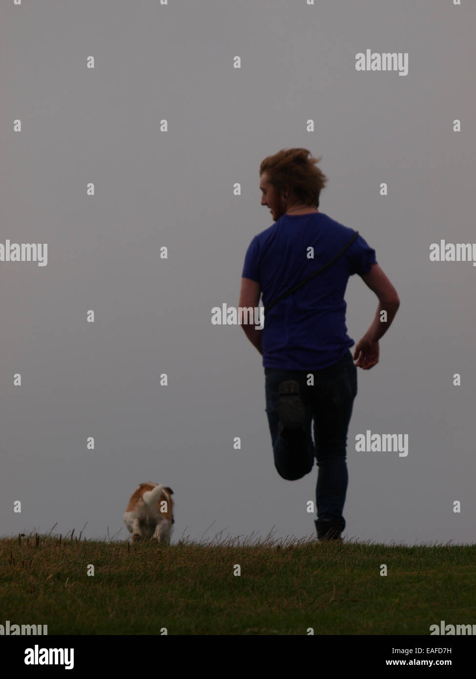 Giovane uomo adulto in esecuzione con il suo cane, Bude, Cornwall, Regno Unito Foto Stock