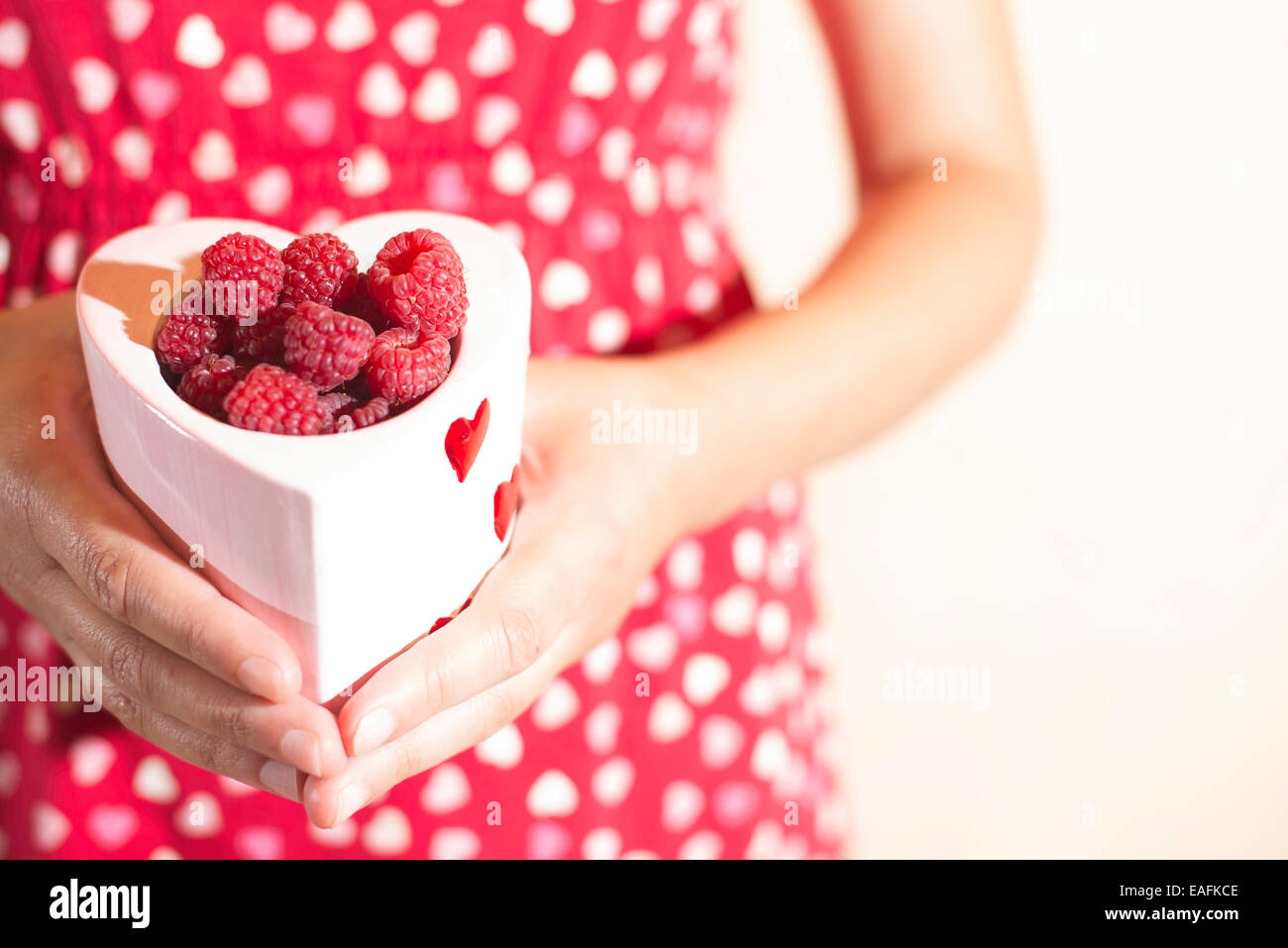 Donna in abito rosso tenendo una tazza di lamponi Foto Stock