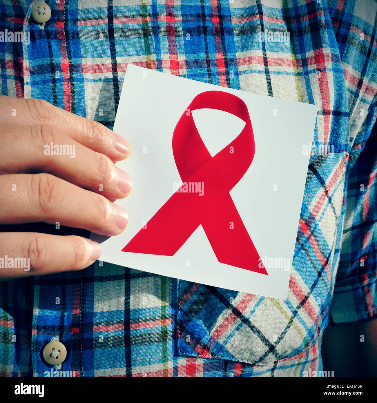 Un giovane uomo in possesso di una immagine di un nastro rosso per la lotta contro l AIDS, sul suo petto Foto Stock