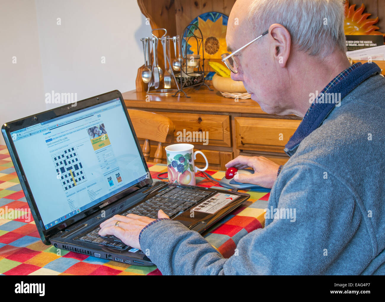 Uomo in pensione per risolvere un cruciverba usando un computer portatile. Foto Stock