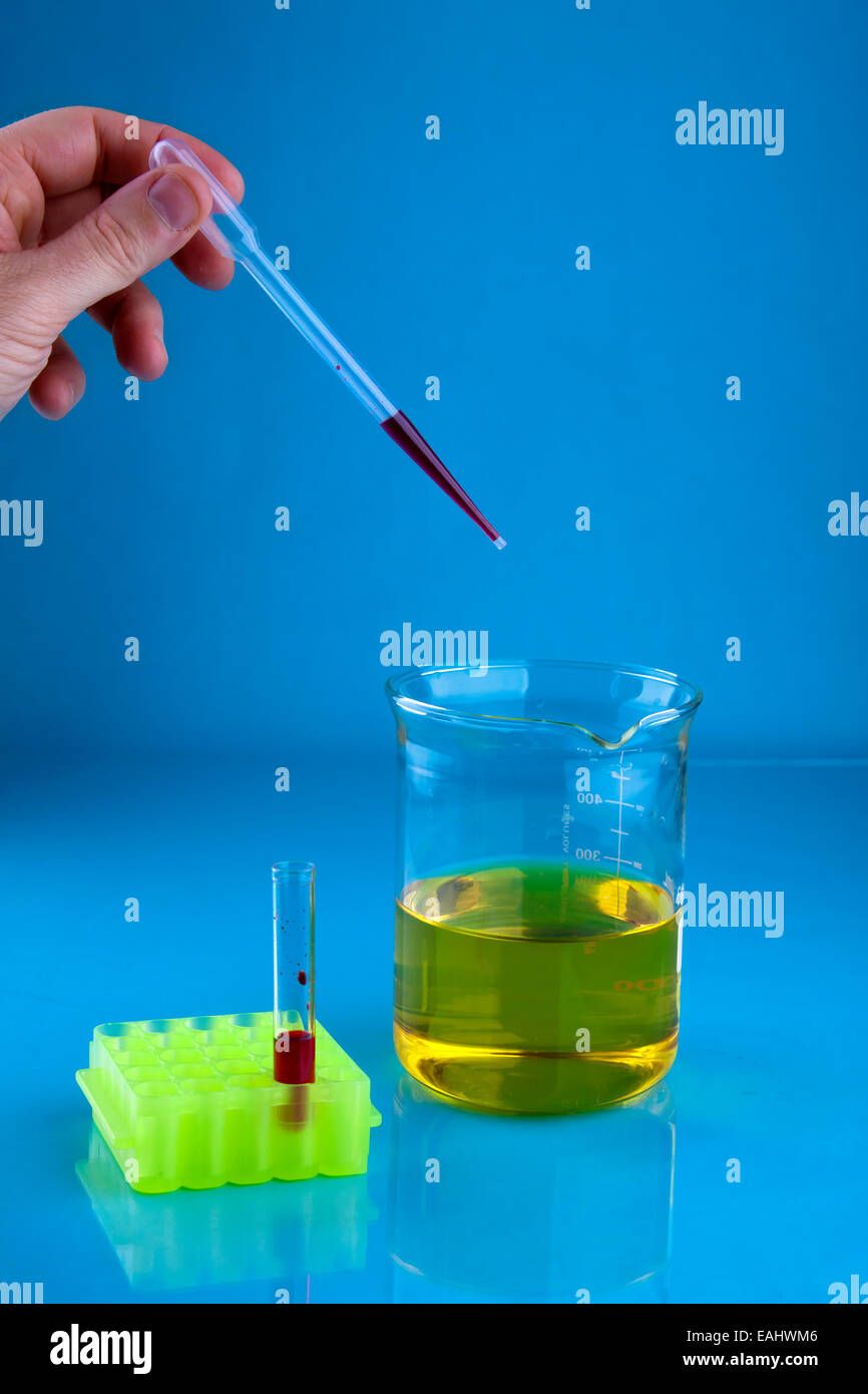 Il pipettaggio di colorante rosso in un bicchiere contenente un liquido giallo. Foto Stock