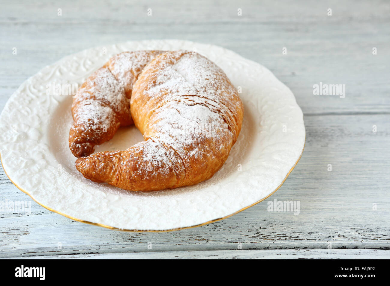 Deliziosi croissant su una piastra, su assi di legno Foto Stock