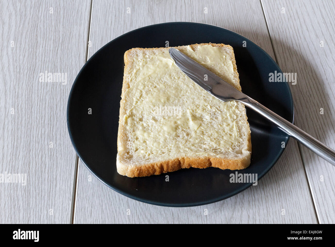 Pezzo di bianco imburrato fette di pane su una piastra con un coltello Foto Stock