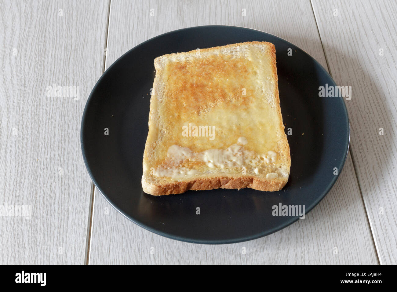 Pezzo di imburrato del pane tostato caldo su di una piastra Foto Stock