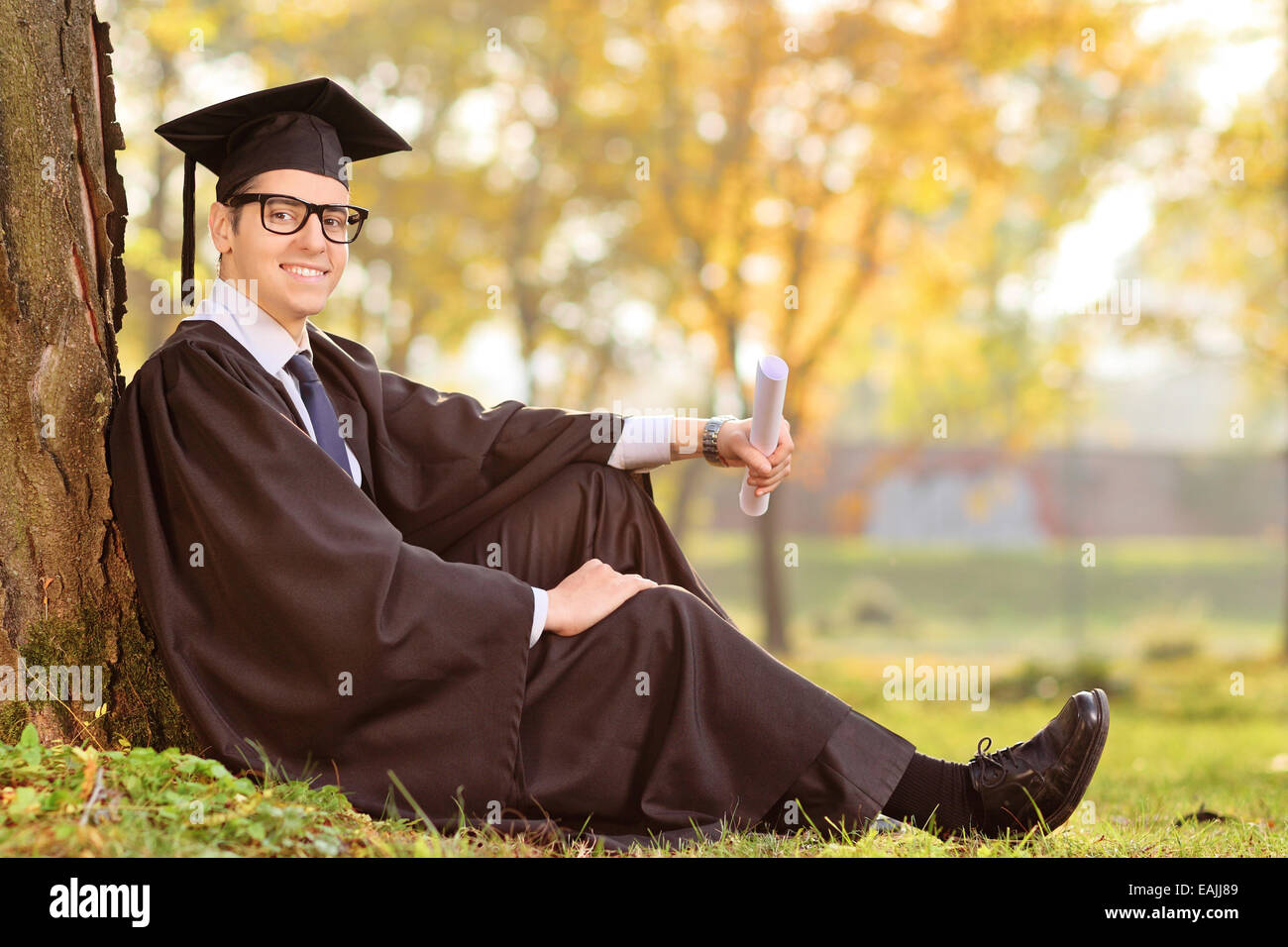 Studente laureato seduto da un albero in un parco Foto Stock