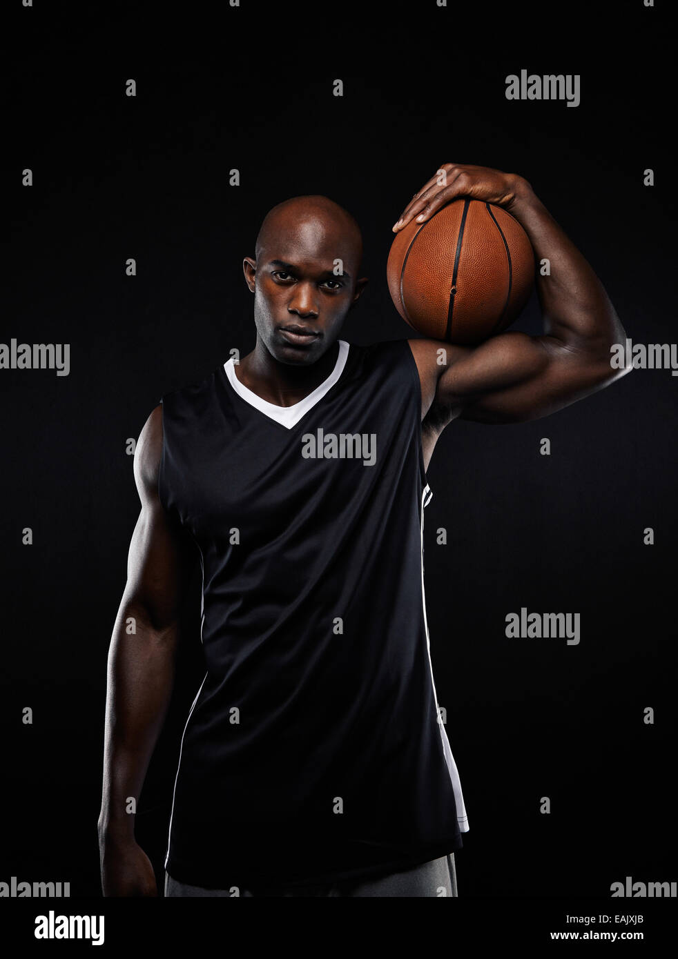 Ritratto di giocatore di pallacanestro professionale tenendo la palla sulle sue spalle contro lo sfondo nero. Foto Stock