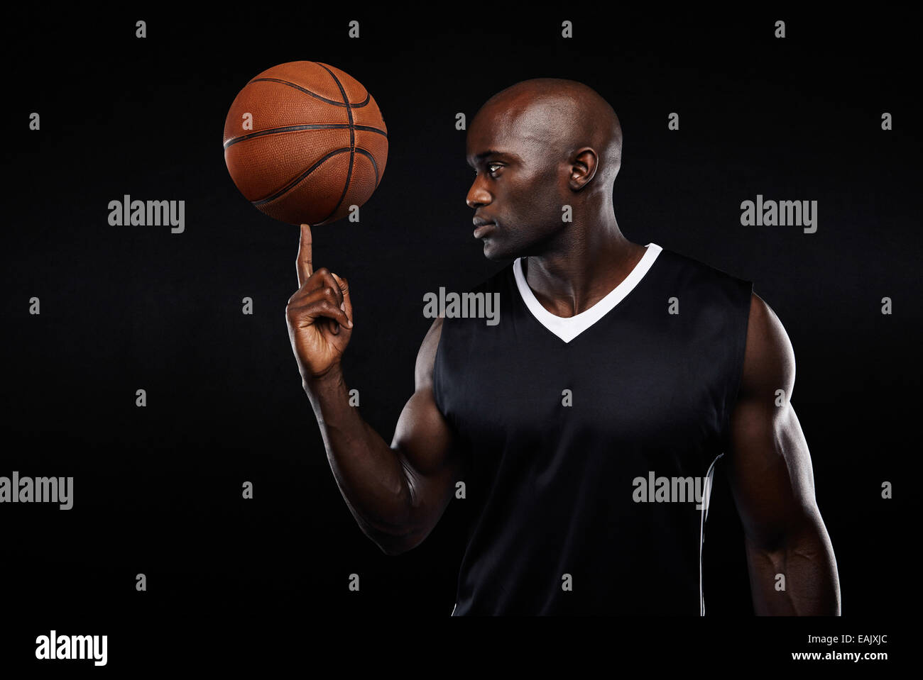 Ritratto di giovane africano atleta di pallacanestro di bilanciamento sul suo dito su sfondo nero. Focalizzato giocatore di basket. Foto Stock