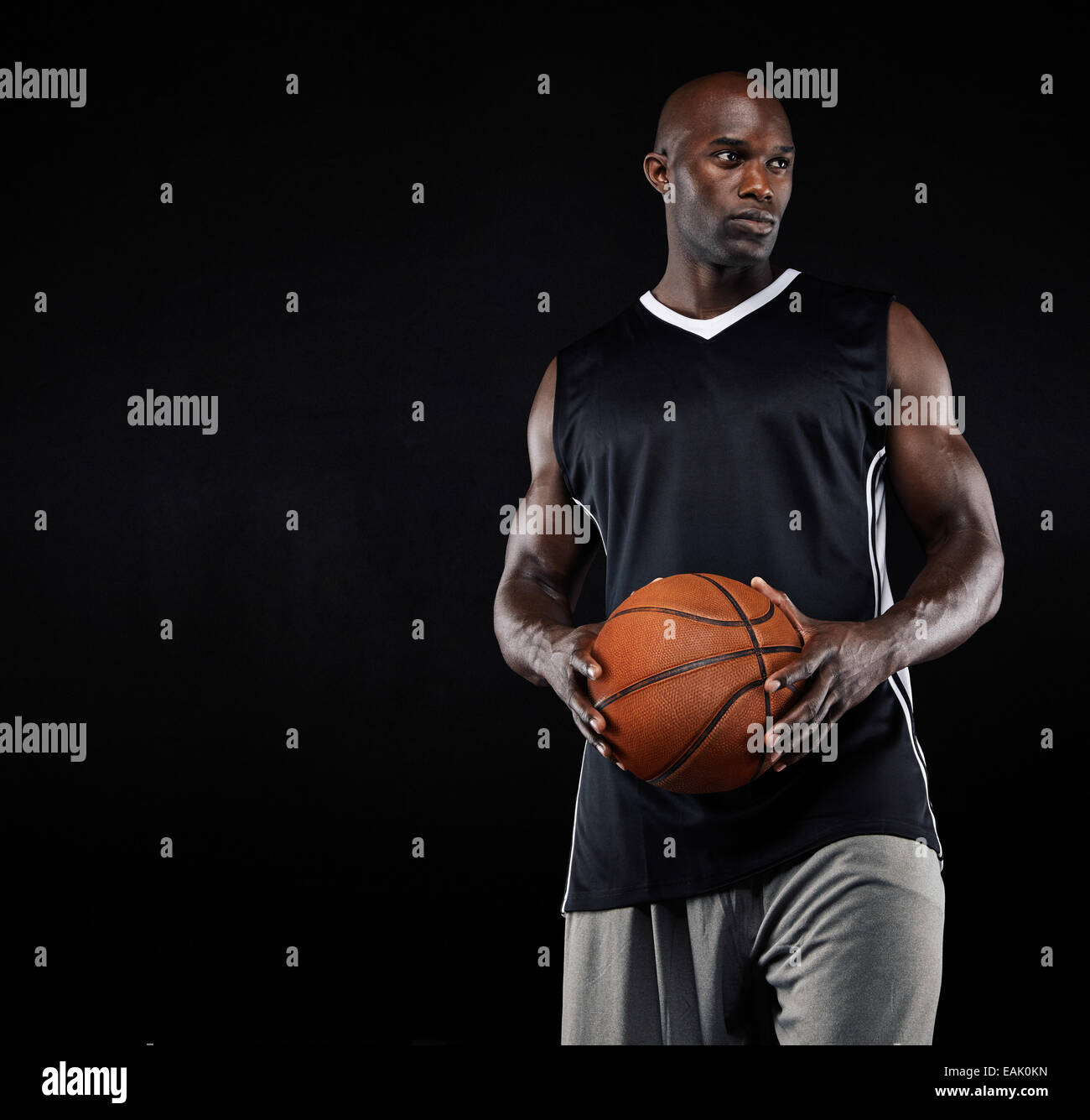 Studio shot di nero giocatore di basket con la sfera che guarda lontano contro lo sfondo nero. Forte giovane con la pallacanestro. Foto Stock