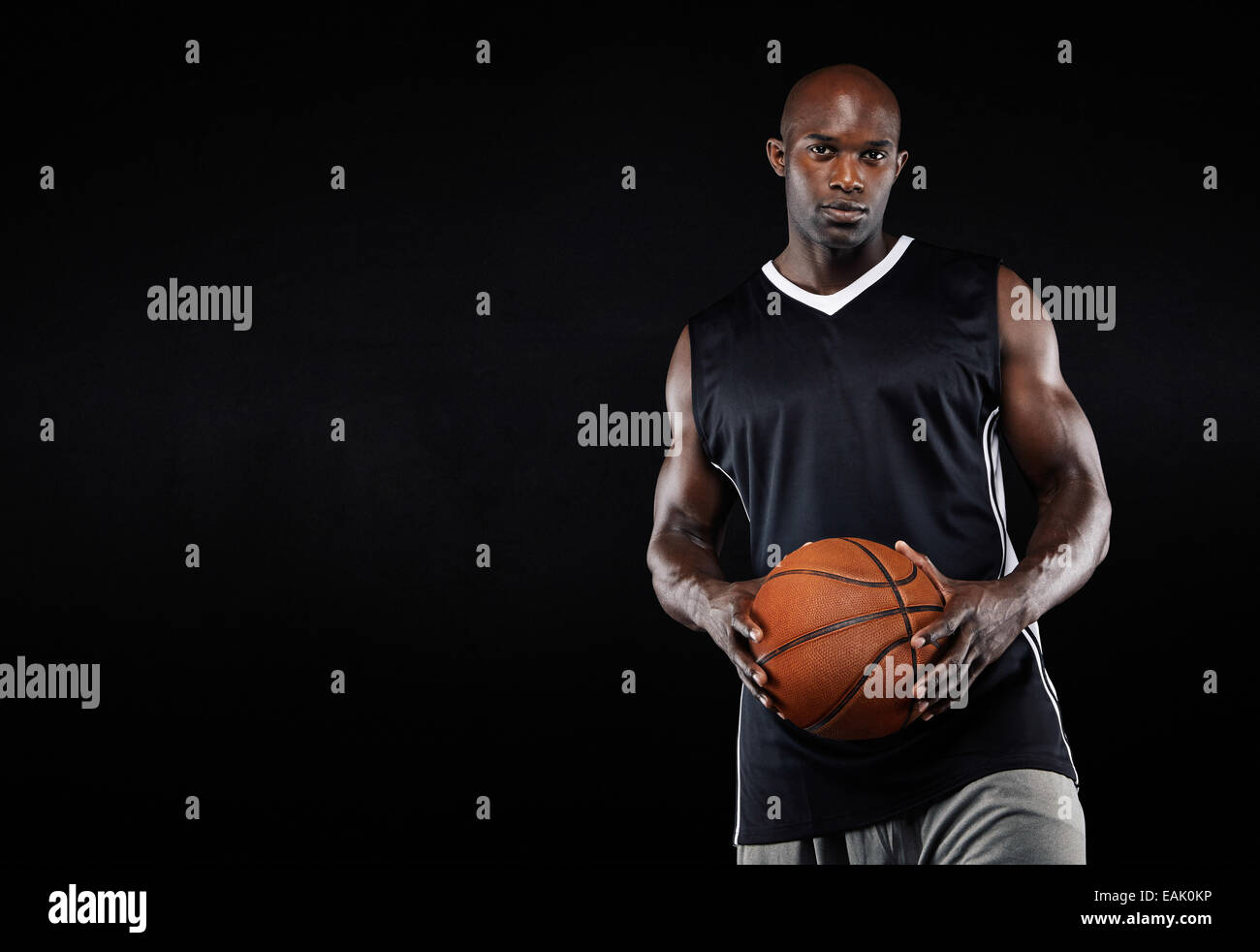 Studio shot di un giovane giocatore di basket in piedi con il suo basket. L'uomo africano tenendo una palla da basket su sfondo nero Foto Stock