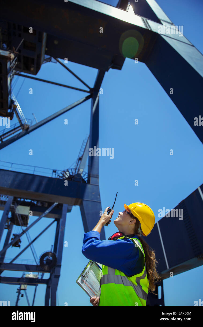 Basso angolo vista del lavoratore utilizzando un walkie-talkie sotto la gru di carico Foto Stock