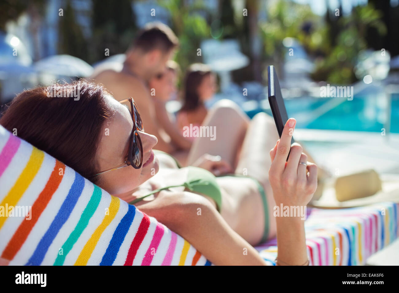 La donna a prendere il sole e i messaggi di testo da piscina Foto Stock