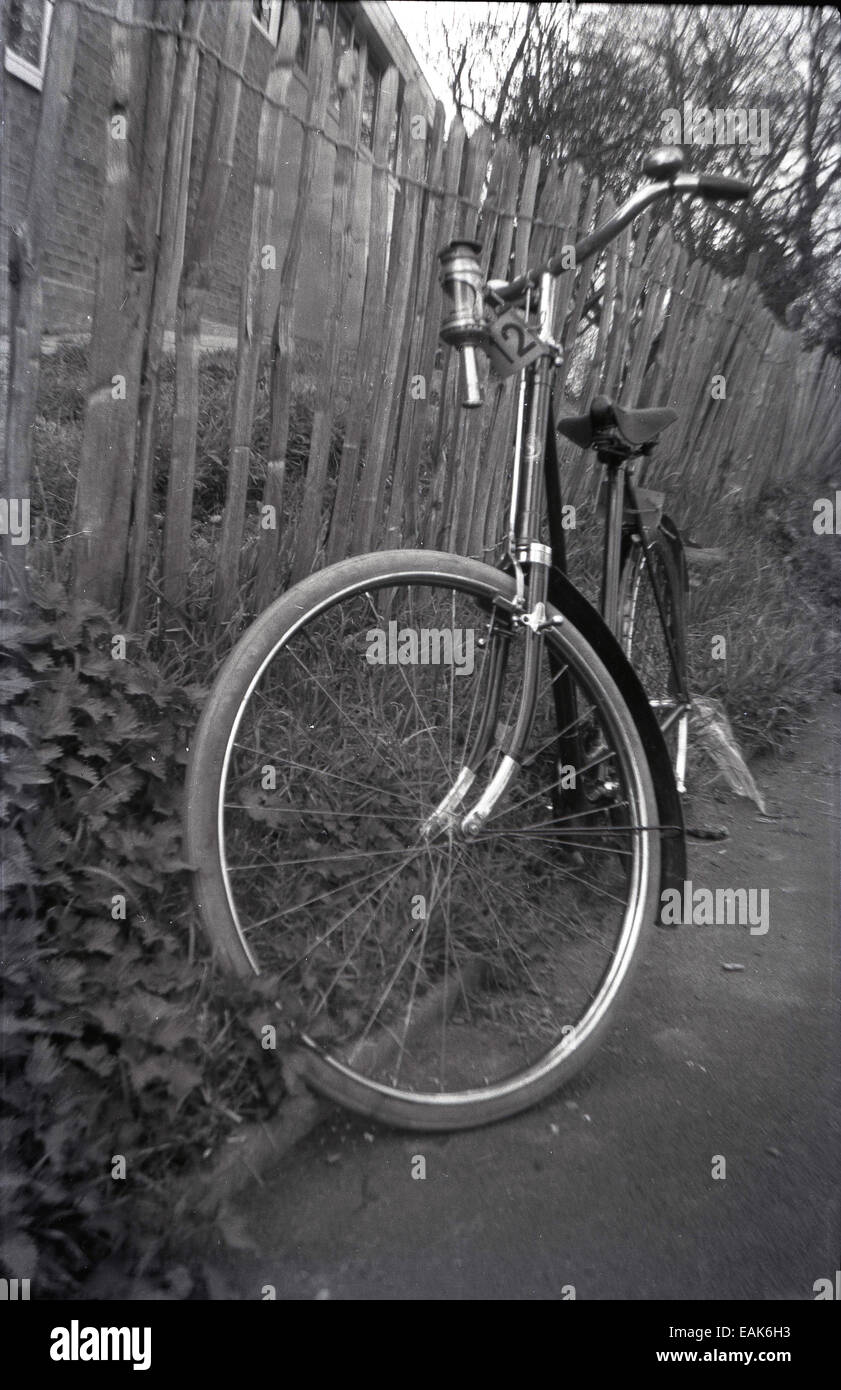 Anni '70, una bicicletta tradizionale in stile dutchie con manubrio alto, posizione seduta verticale e passo attraverso telaio parcheggiato contro una recinzione in legno ardesia, Inghilterra, Regno Unito. Foto Stock