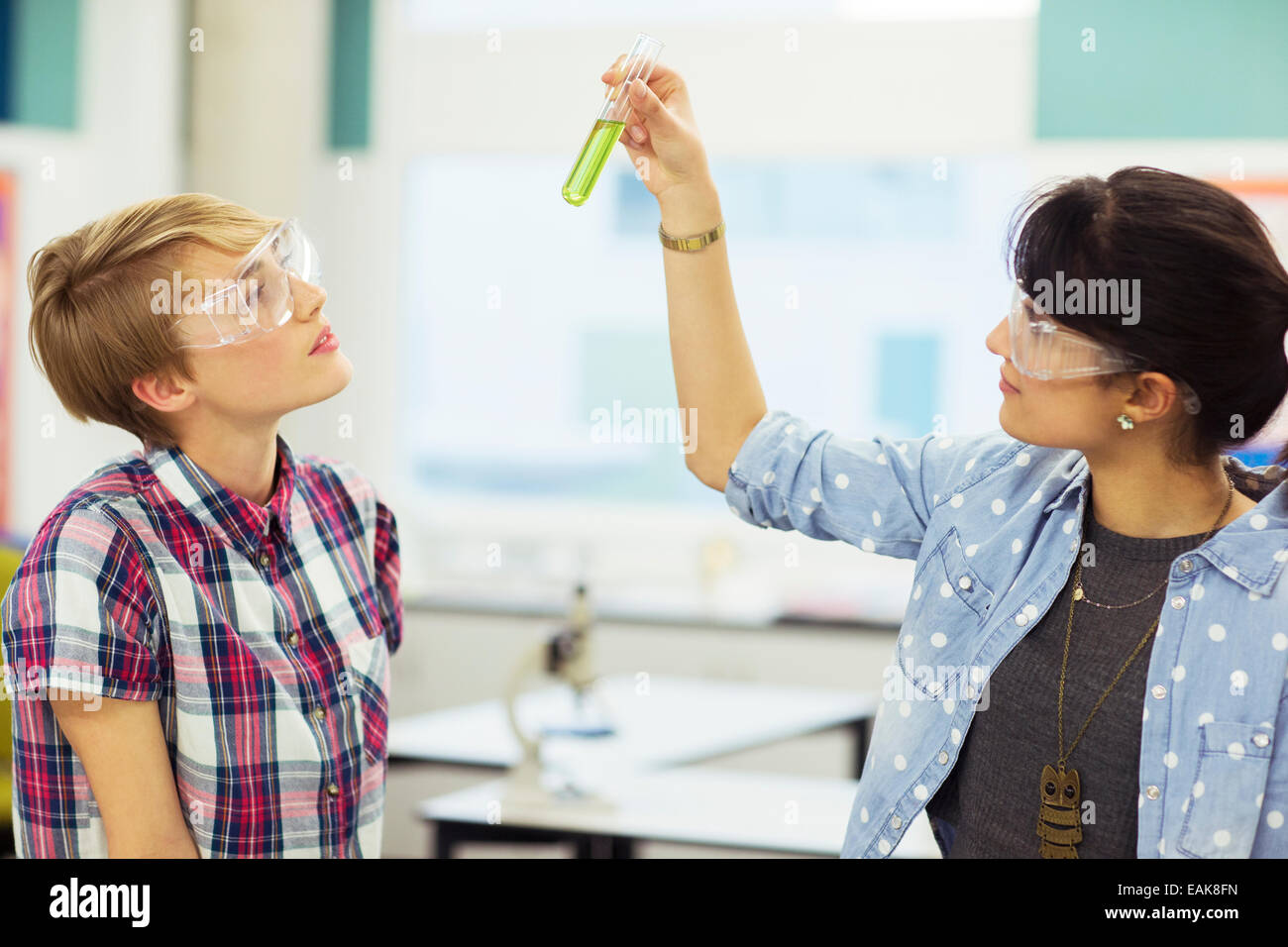 Insegnante e studente durante la lezione di Chimica, indossare occhiali protettivi e guardando il tubo di prova con liquido verde Foto Stock