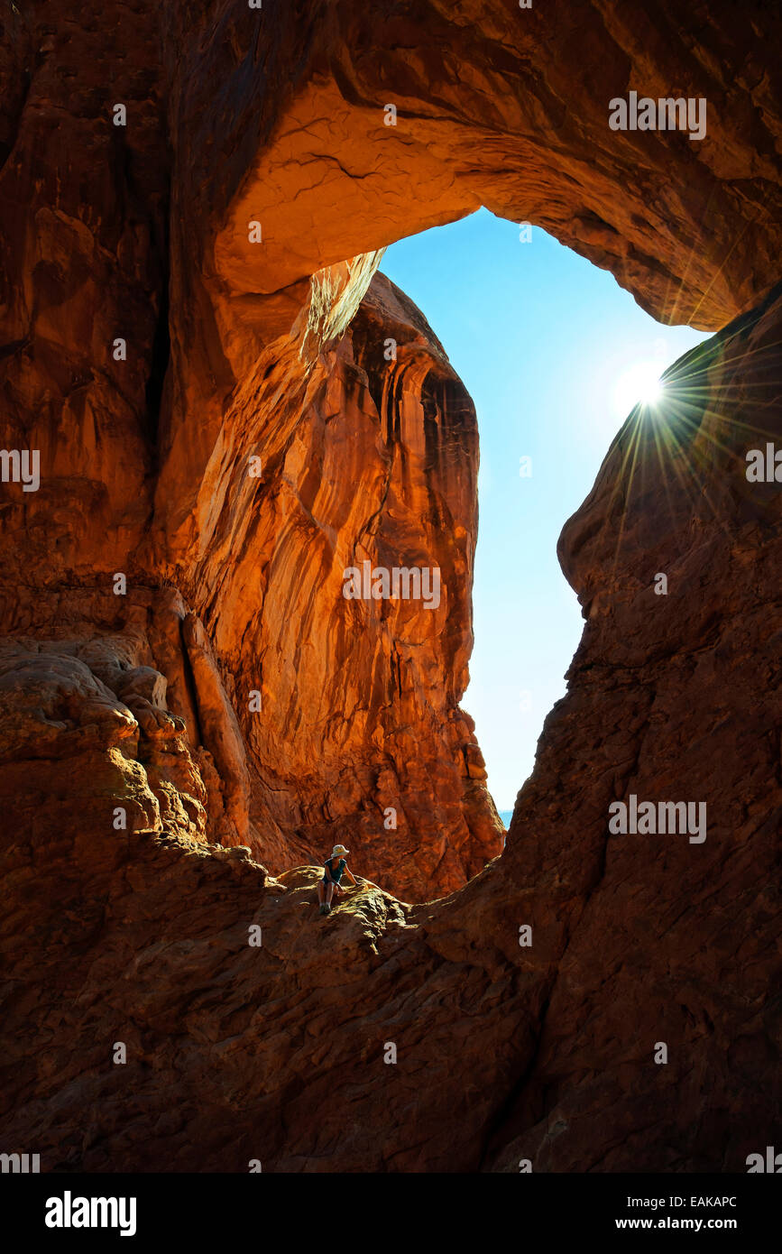 Escursionista rilassante sotto il doppio arco, archi in pietra di arenaria rossa formata da erosione, Arches-Nationalpark, vicino a Moab, Utah Foto Stock