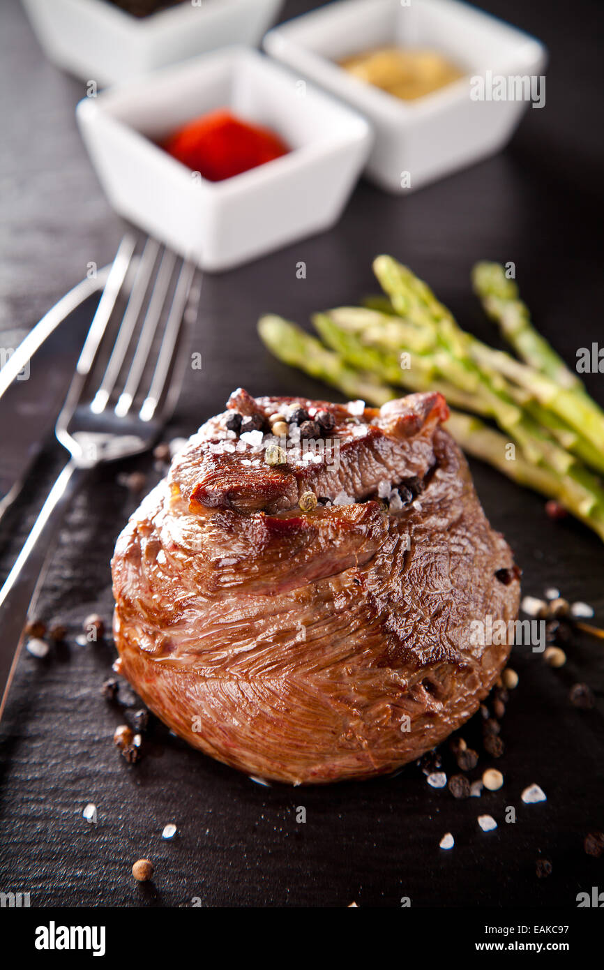 Pezzo di carne rossa bistecca con rosmarino servita sulla pietra nera superficie. Foto Stock