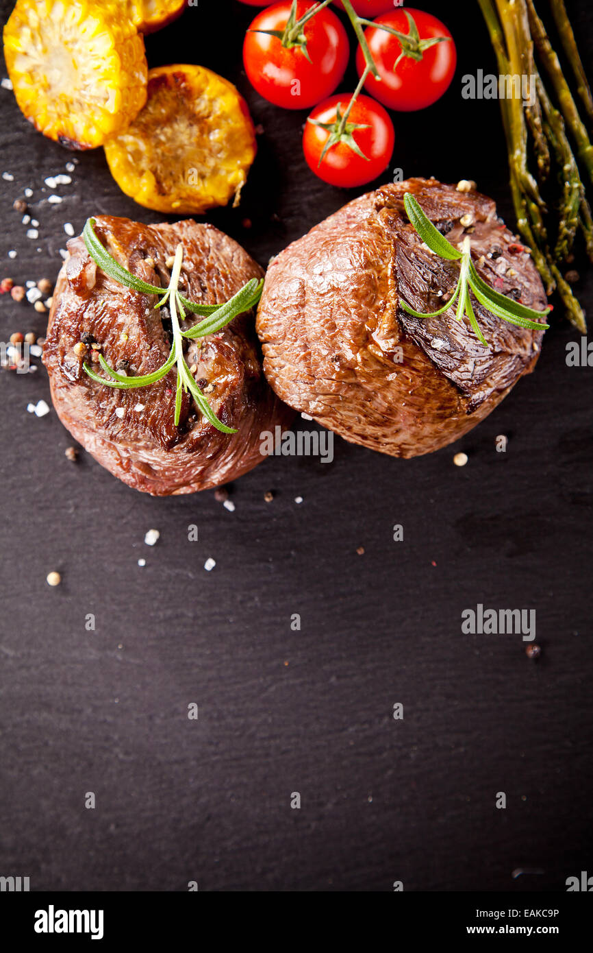 Pezzi di carne rossa bistecche con verdure e spezie, servito su pietra nera superficie. Scattato dalla vista superiore Foto Stock