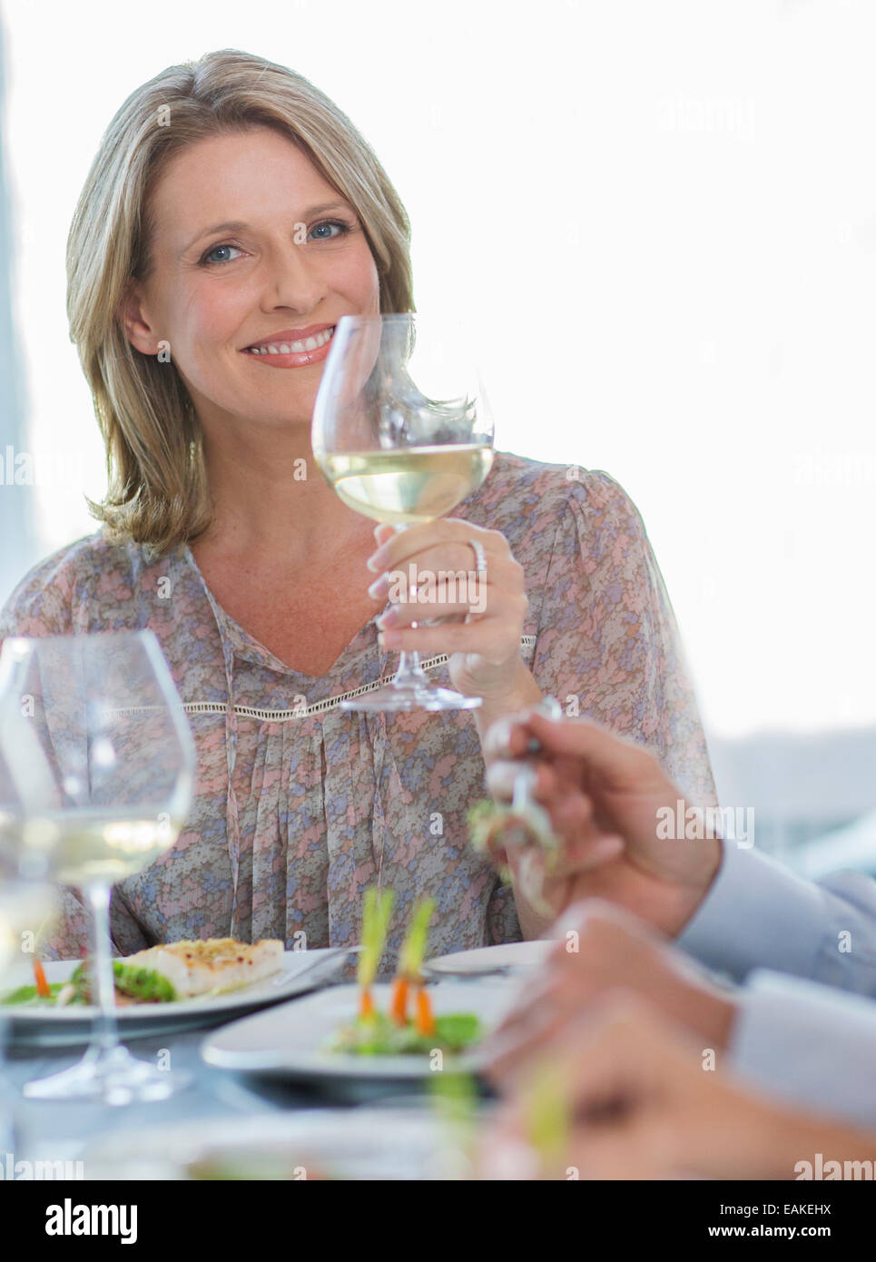 Ritratto di donna sorridente tenendo un bicchiere di vino bianco presso il ristorante la tabella Foto Stock