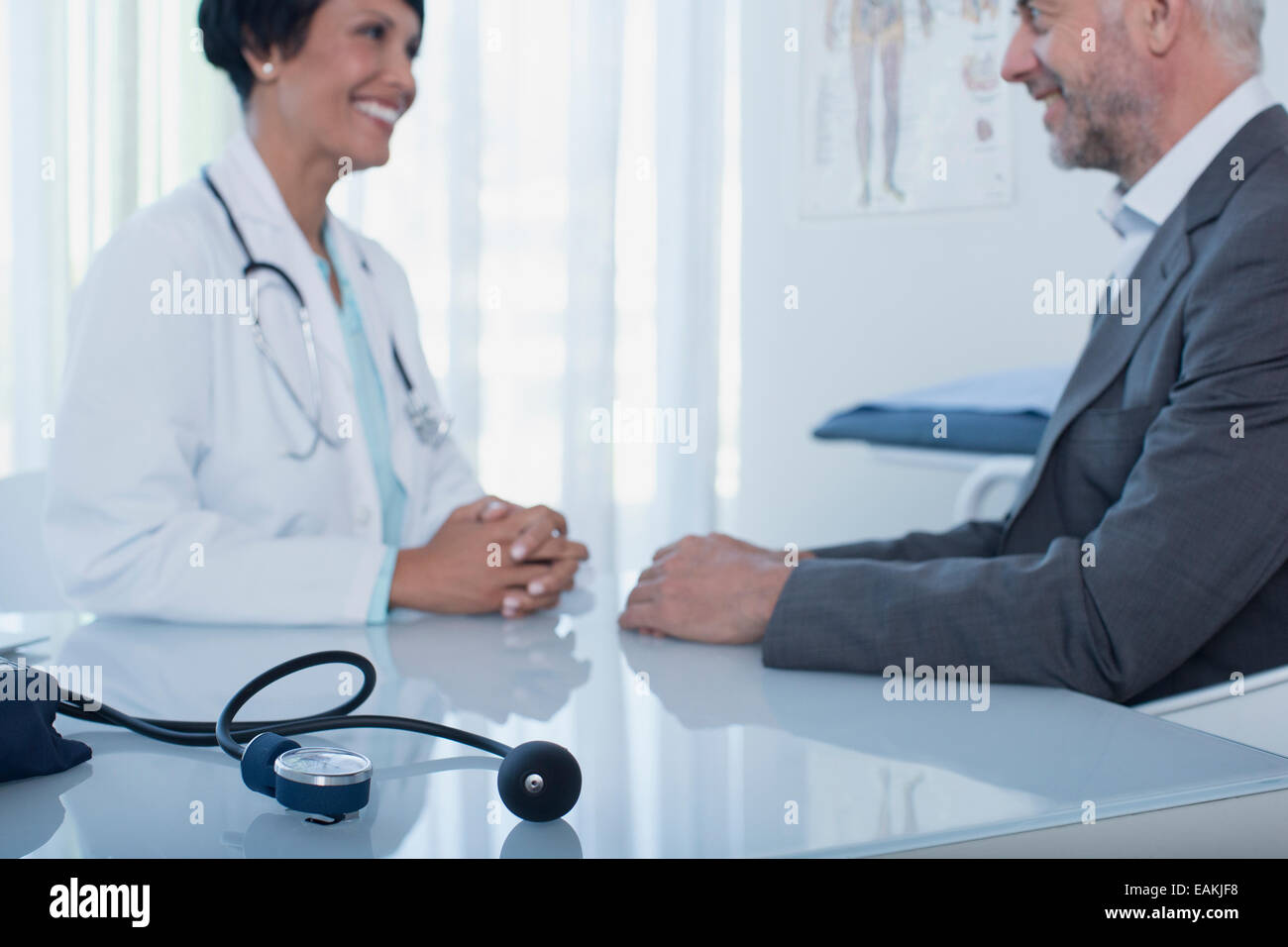 Donna sorridente medico parlando al paziente alla scrivania in ufficio, la pressione del sangue il manometro in primo piano Foto Stock