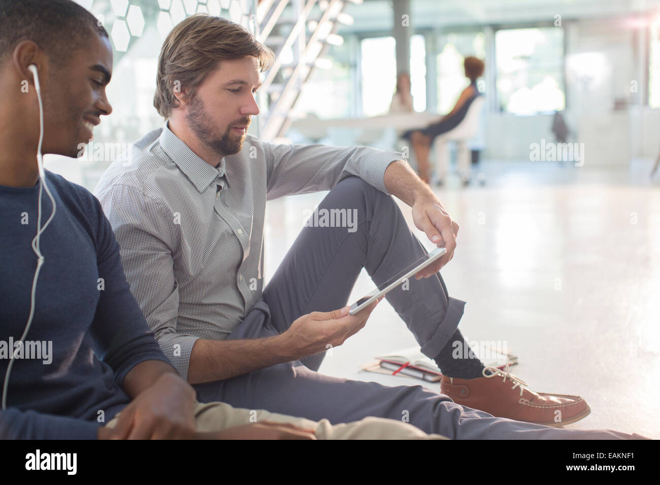 Due imprenditori con tavoletta digitale e gli auricolari in seduta sul pavimento in un ufficio moderno Foto Stock