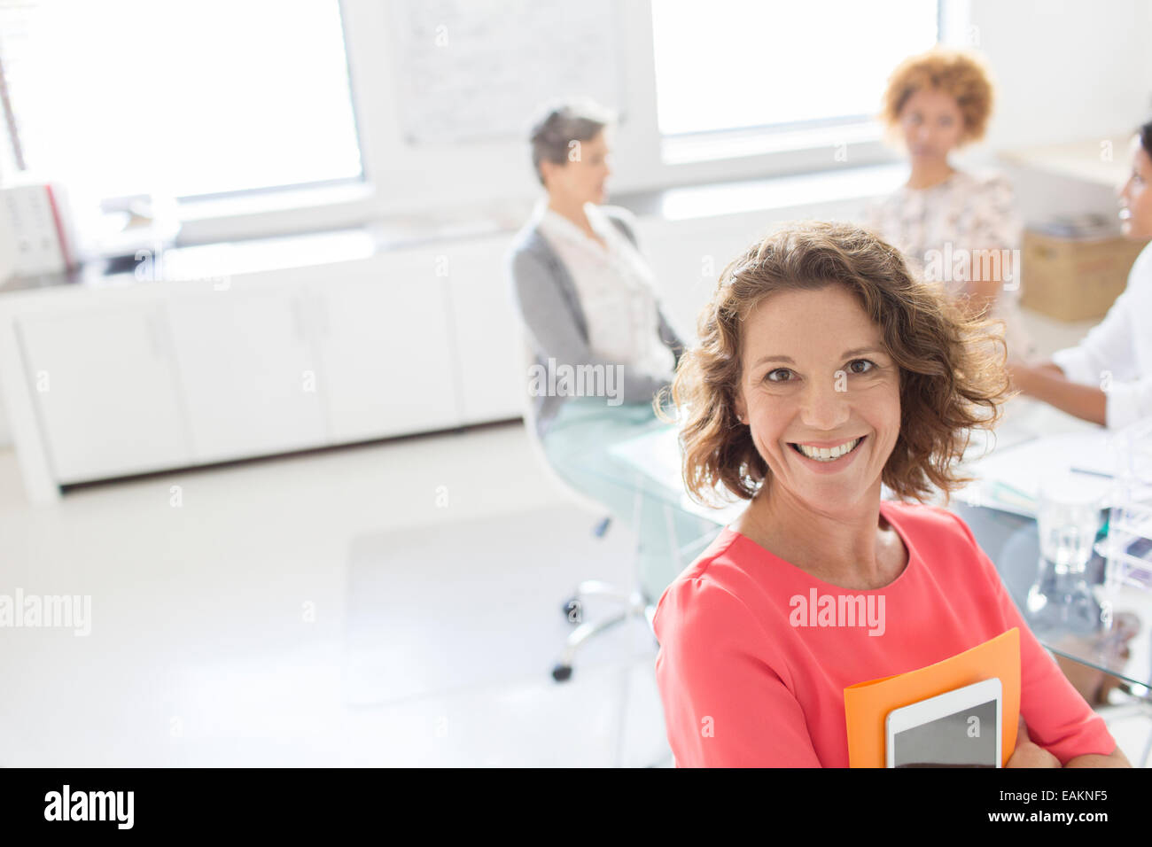 Ritratto di imprenditrice sorridente in ufficio, i colleghi in background Foto Stock