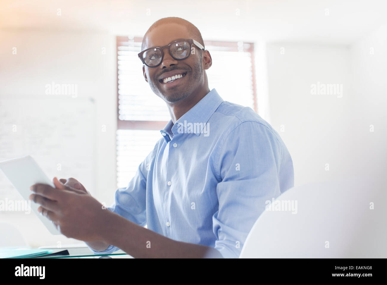 Ritratto di giovane imprenditore con gli occhiali e la maglietta blu holding digitale compressa in office Foto Stock