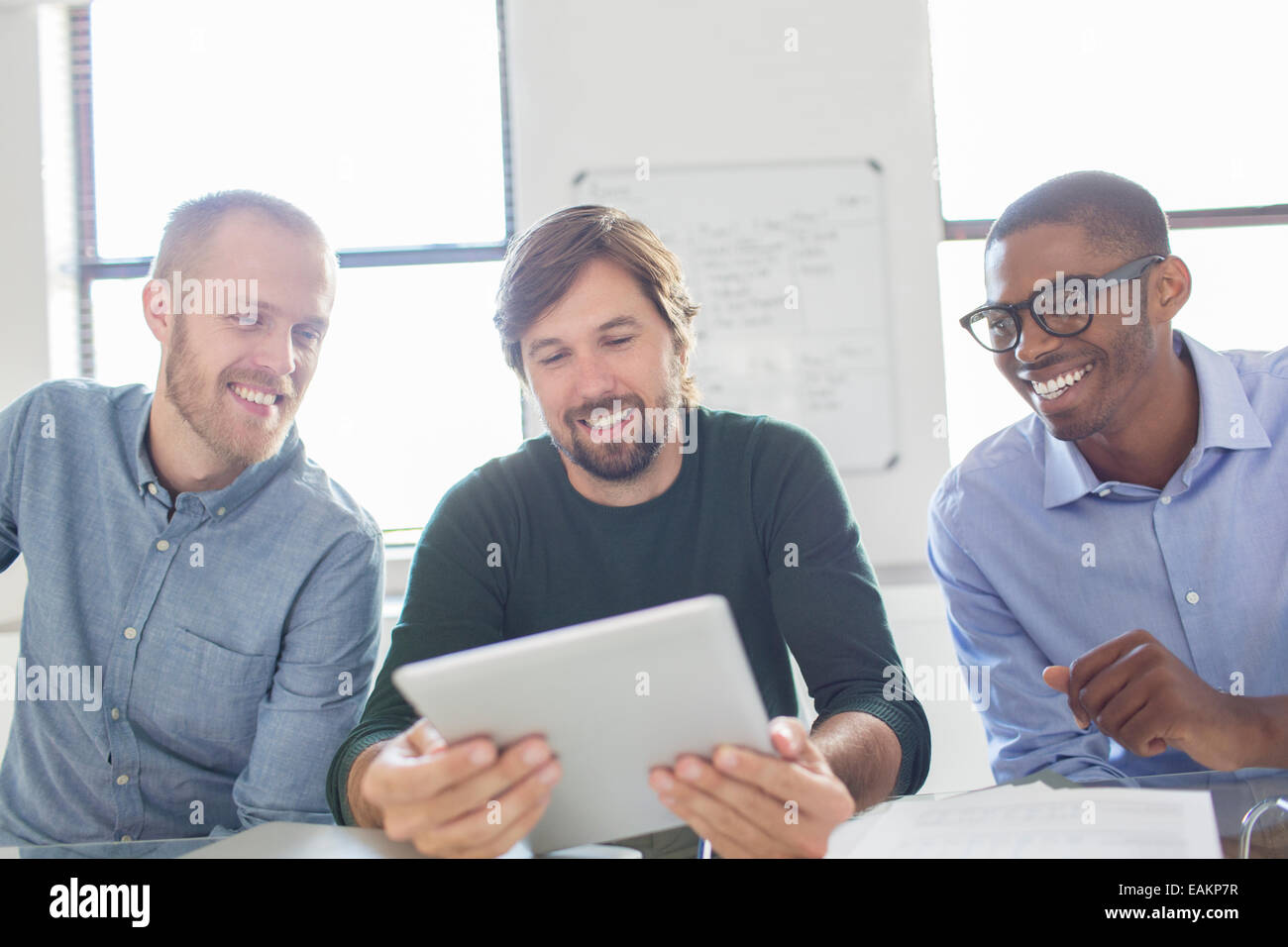 Tre uomini sorridenti lavora con tavoletta digitale in ufficio Foto Stock