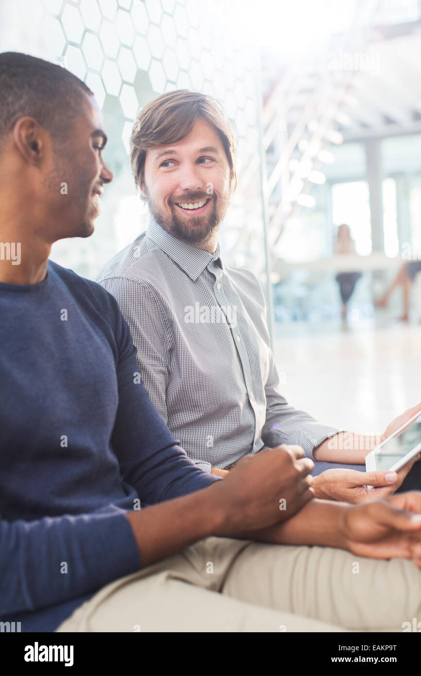 Due uomini sorridenti parlando, tenendo digitale compressa nel corridoio di office Foto Stock