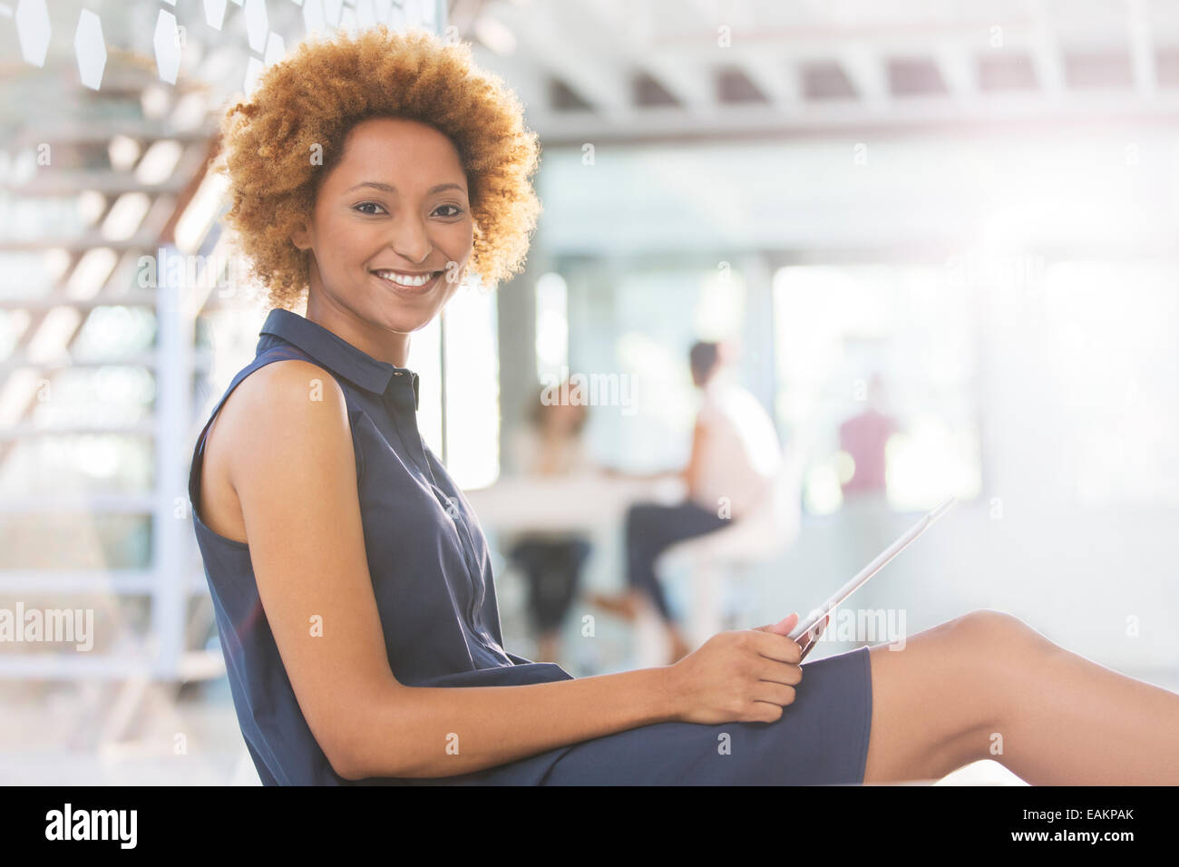 Ritratto di donna sorridente con tavoletta digitale nel corridoio di ufficio, i colleghi in background Foto Stock