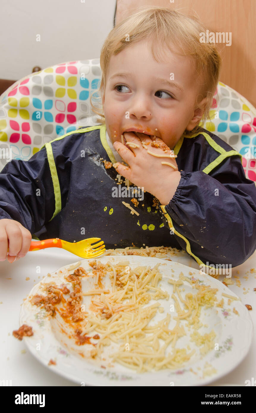Un piccolo ragazzo (ca. 2 anni) mangia un piatto di spaghetti e salsa di pomodoro. Foto Stock