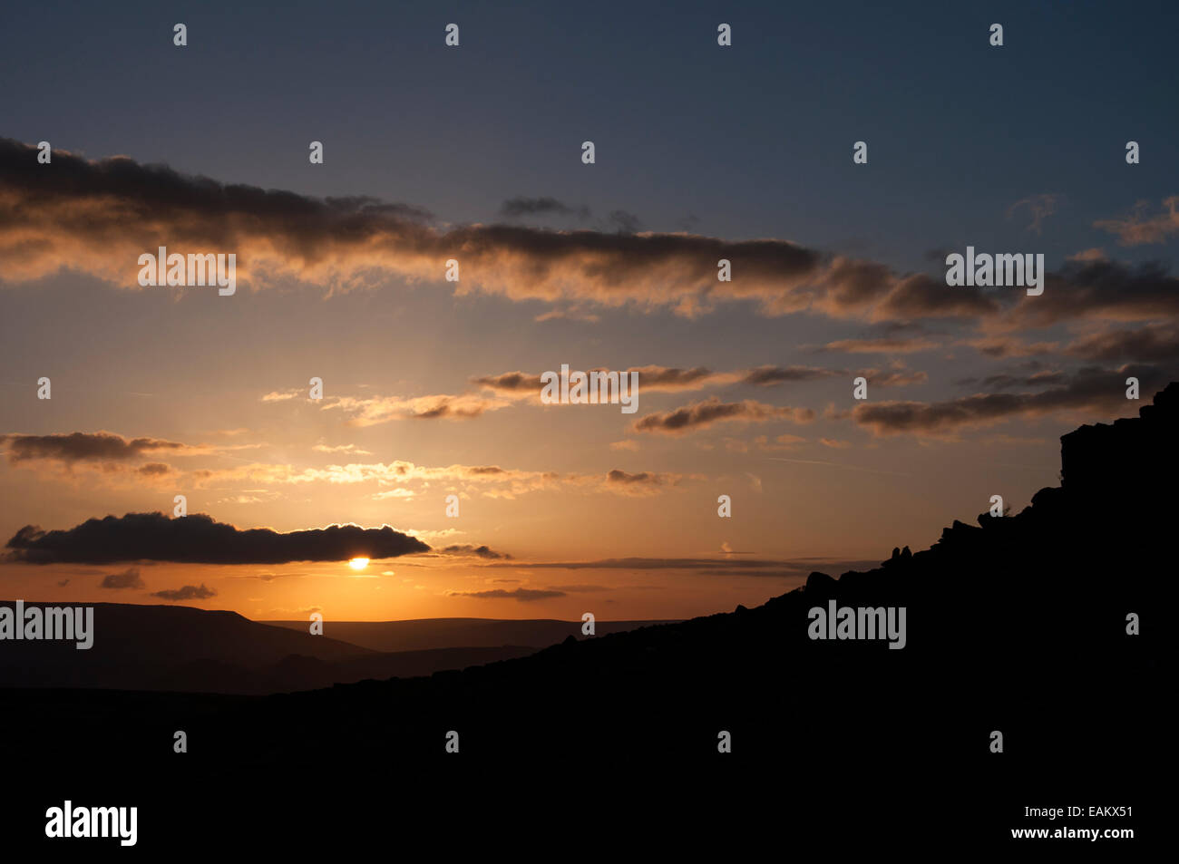 Bel tramonto a bordo Stanage nel Peak District, Derbyshire. Sun spiata da dietro il cloud e bordo roccioso in silhouette. Foto Stock