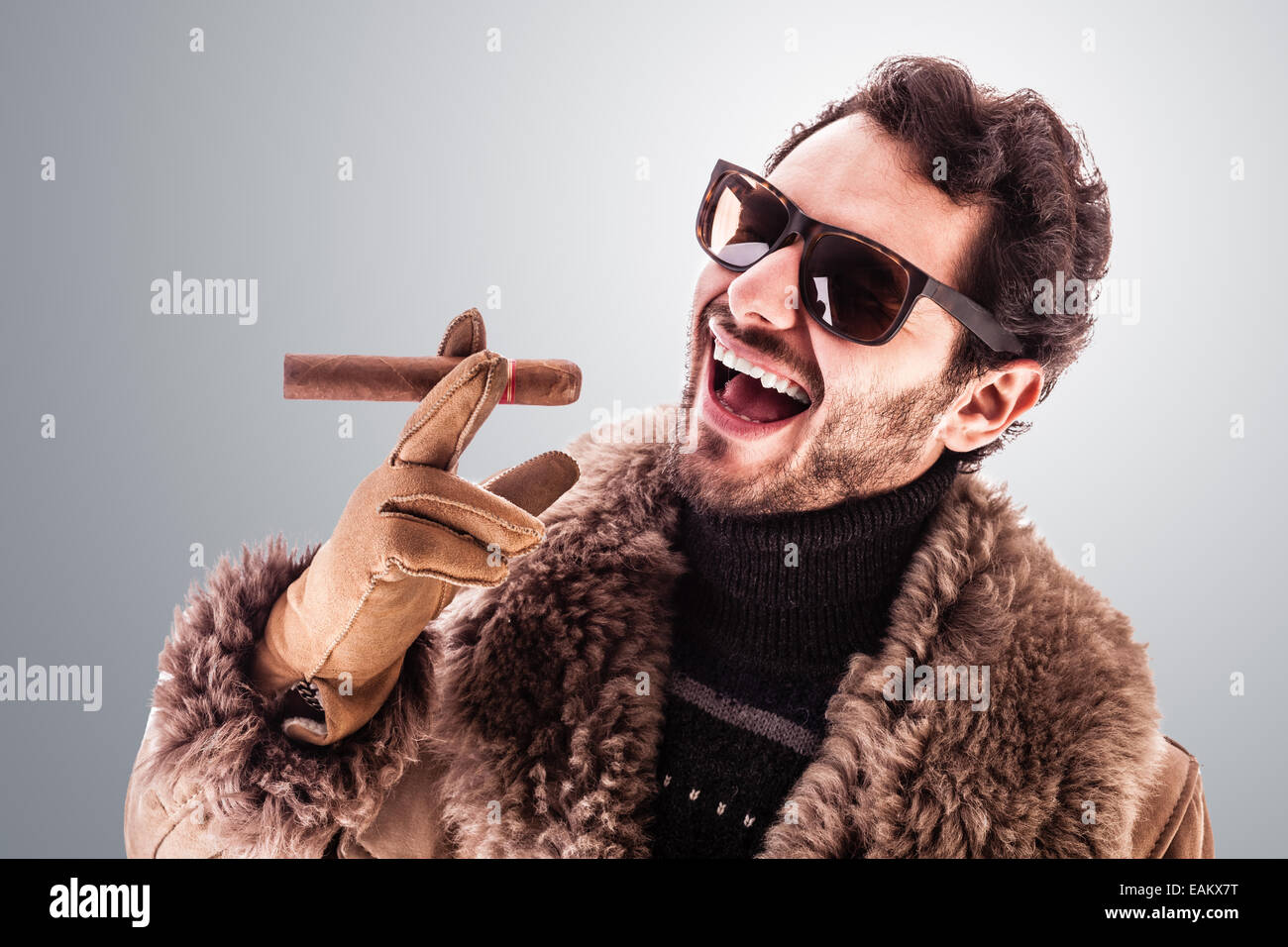 Un giovane e ricco uomo che indossa un cappotto di pelle di pecora isolate su uno sfondo bianco tenendo un sigaro Foto Stock