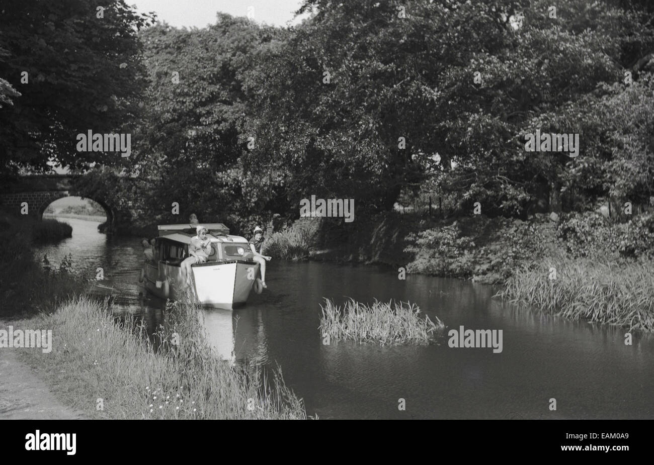 Degli anni Cinquanta, storico, immagine che mostra una barca di piacere sulle rive di un fiume con i ragazzi seduti in barca nella parte anteriore. Foto Stock