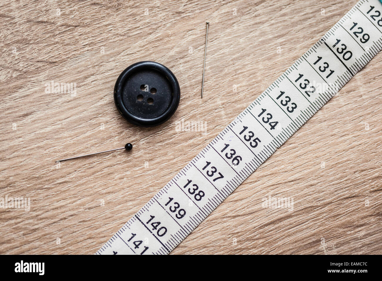 Un pulsante, due aghi da cucire e un nastro di misurazione su una superficie in legno Foto Stock