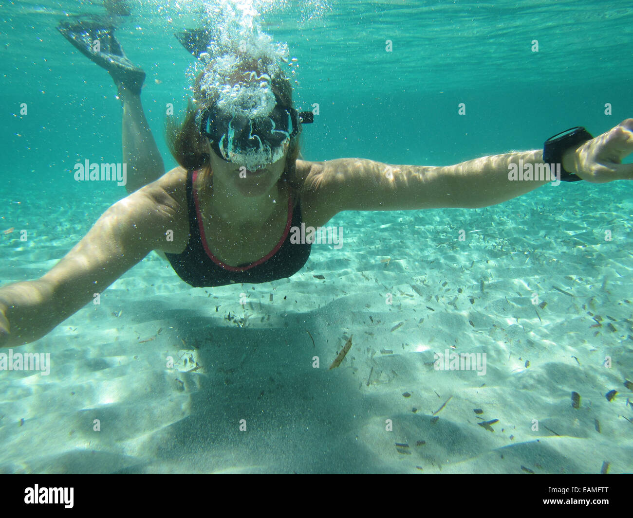 Nuotatore femmina indossando maschera e pinne soffiando bolle di aria nella subacquea ocean su fondo sabbioso Foto Stock