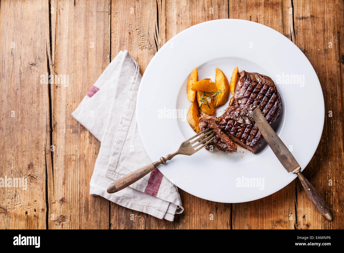 Grigliata di Sud Americano carni bovine Premio New York bistecca con patate arrosto cunei su piastra bianca su sfondo di legno Foto Stock
